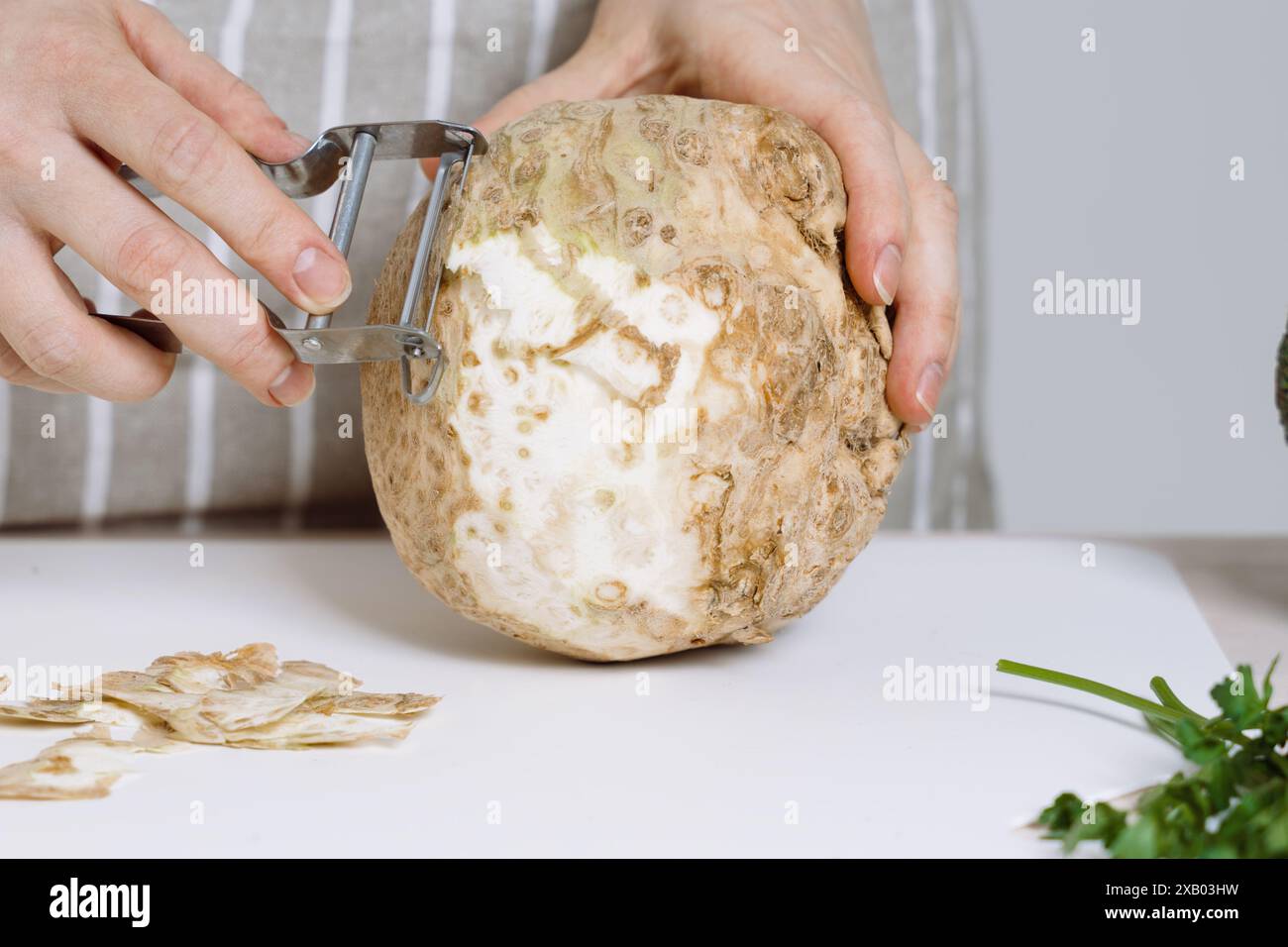 Una donna in grembiule che sbuccia il sedano o la radice di sedano con sbucciatore in cucina. Sedano in zuppe, stufati e ricette sane ricche di antiossidanti e mio Foto Stock