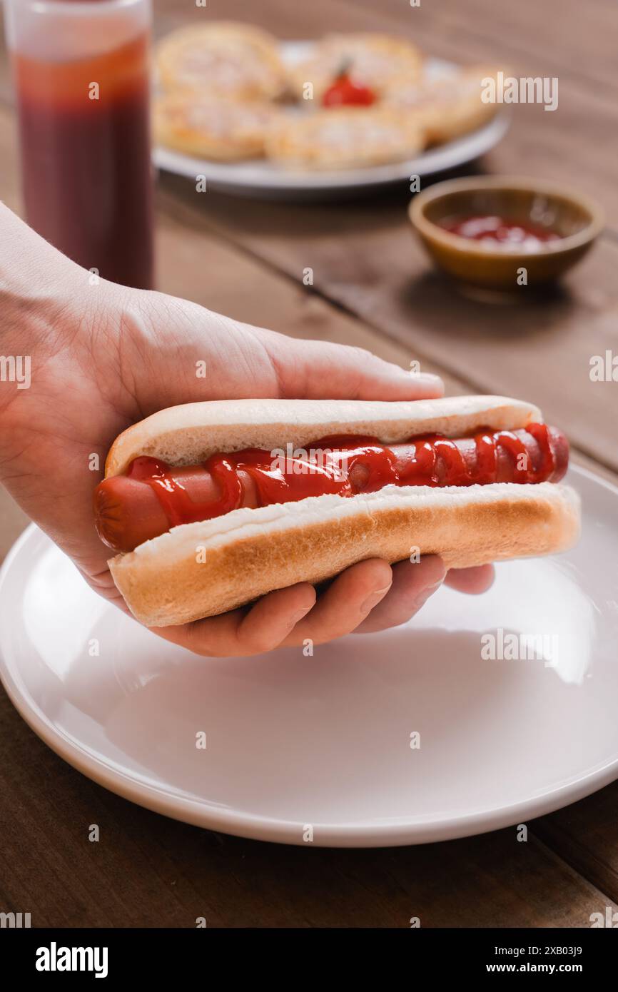 Una persona serve un hot dog con ketchup su un piatto bianco. Questo pasto ad alto contenuto calorico, obesità, salsicce vegane alternative. Foto Stock