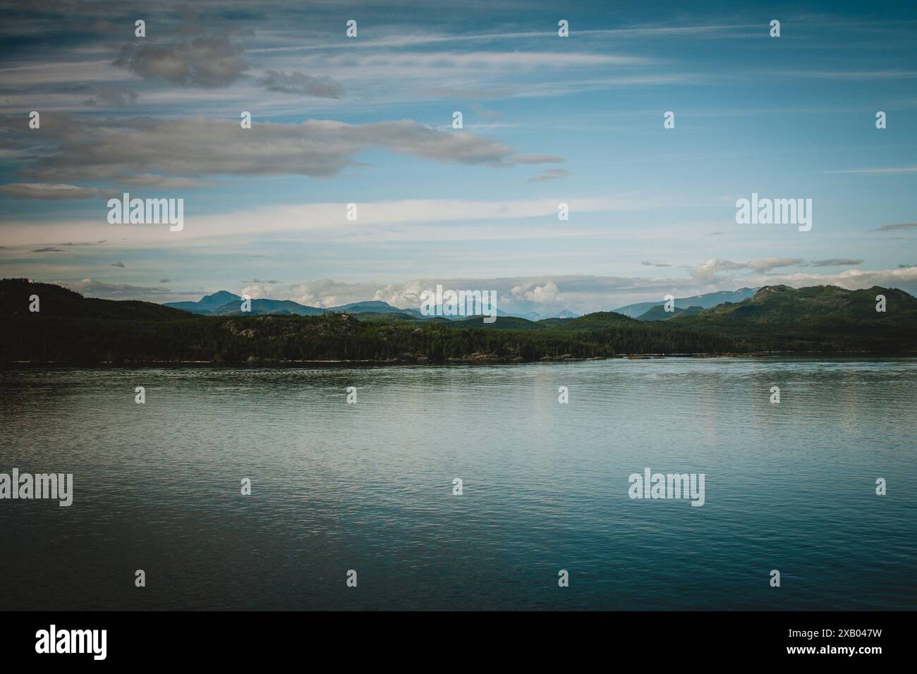 Questa fotografia mozzafiato cattura la serena bellezza della natura selvaggia dell'Alaska, con lussureggianti colline verdi e acque calme sotto un cielo blu cristallino, per Foto Stock