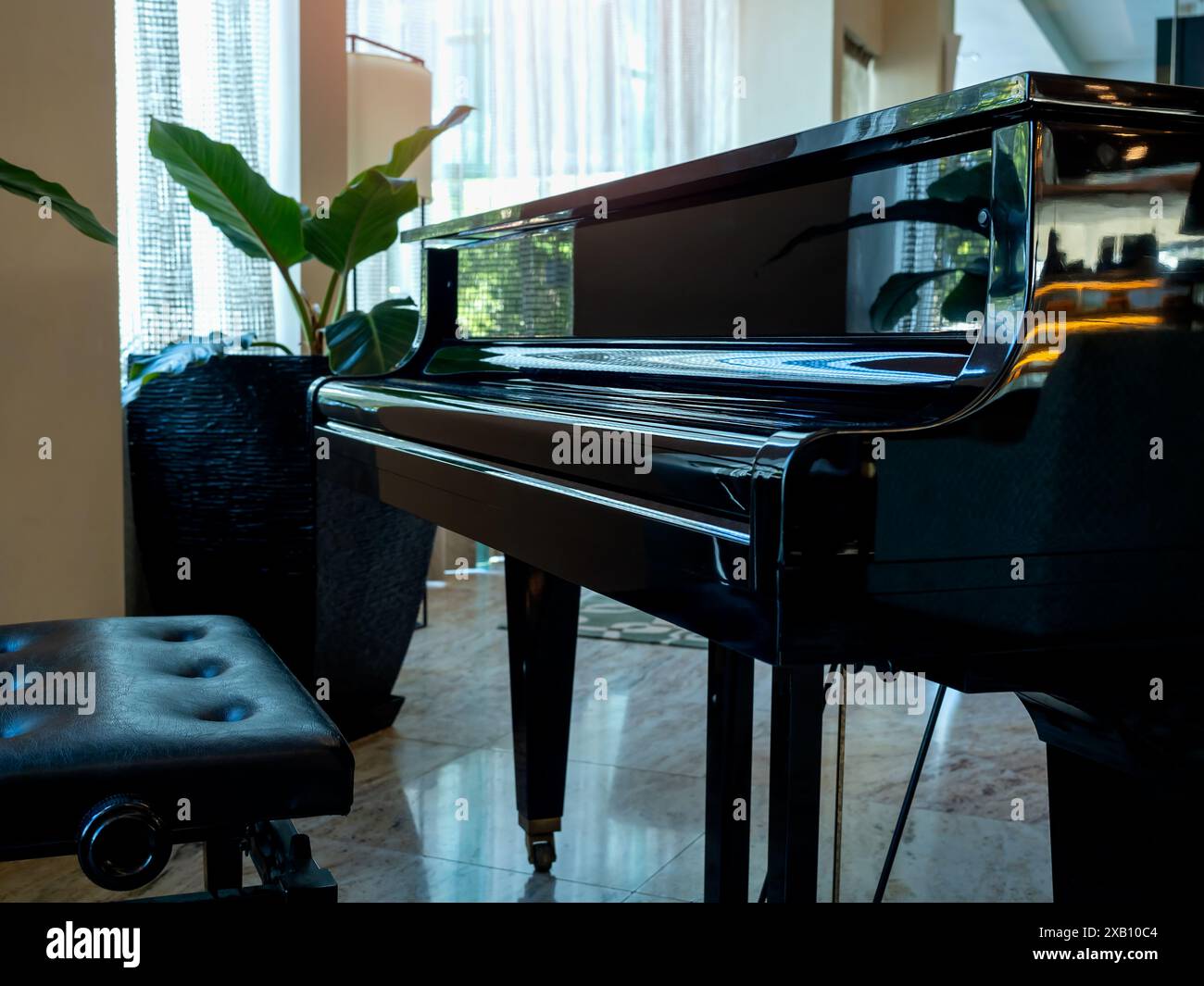 Piano nero ravvicinato, posto vuoto in pelle e vaso vicino a una grande finestra di vetro con tende bianche nella hall o nel ristorante dell'hotel senza nessuno. Foto Stock