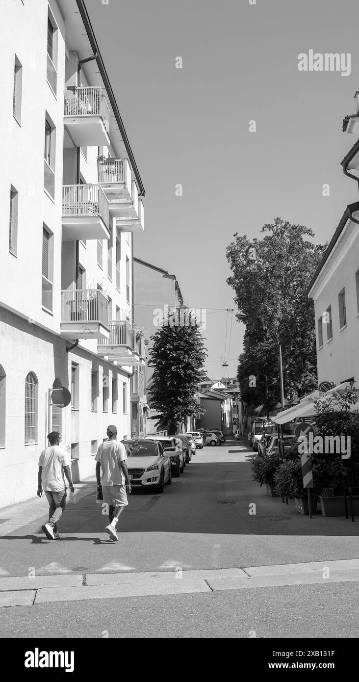 Cremona, Italia - 16 maggio 2024 due giovani si allontanano dalla telecamera lungo una strada stretta con auto parcheggiate su entrambi i lati in una soleggiata estate Foto Stock