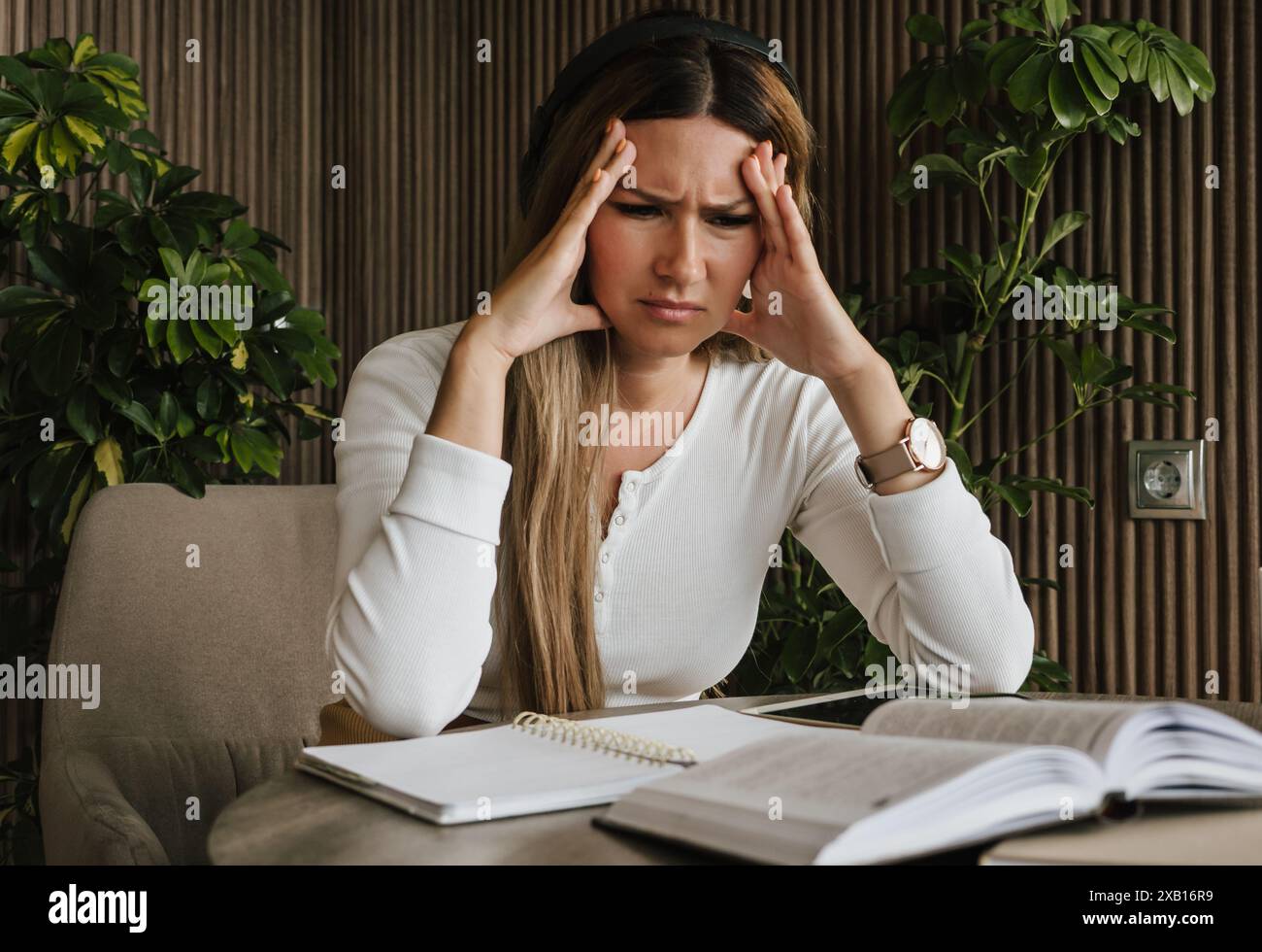 La donna sente lo stress sul lavoro, tenendo la testa in frustrazione mentre è circondata da documenti e appunti. Pressione professionale e stress mentale. Stress sul posto di lavoro, salute mentale e concetto di vita d'ufficio. Foto Stock