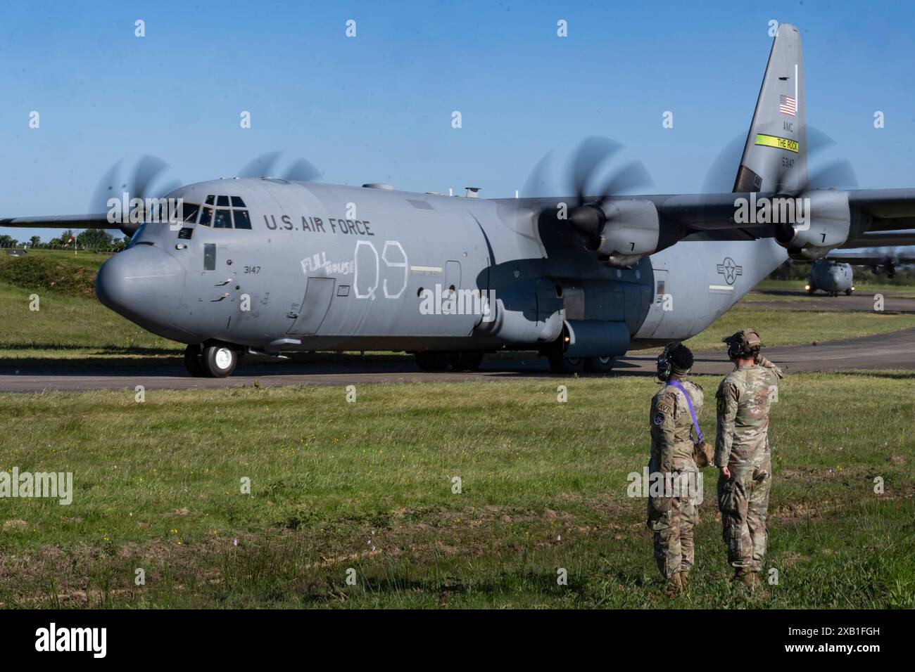 Due capi dell'equipaggio degli aviatori della U.S. Air Force salutano un C-J130 Hercules a sostegno del 80° anniversario del D-Day a Cherbourg - Maupertus Airport, Francia, J Foto Stock