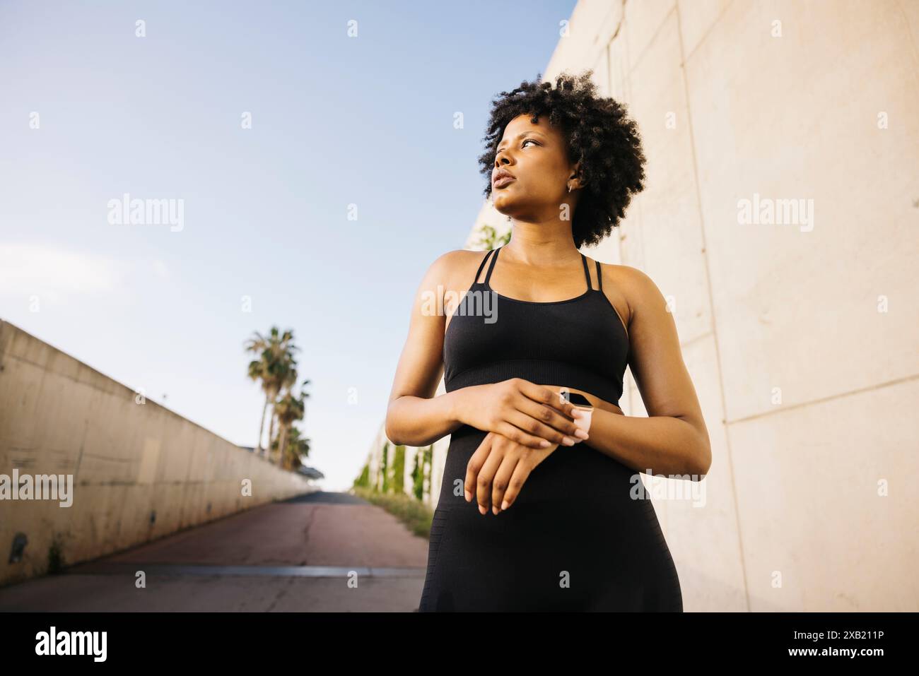 Donna che guarda in lontananza mentre è in piedi per strada prima di allenarsi. Giovane donna che indossa abiti sportivi per preparare il suo esercizio all'aperto Foto Stock