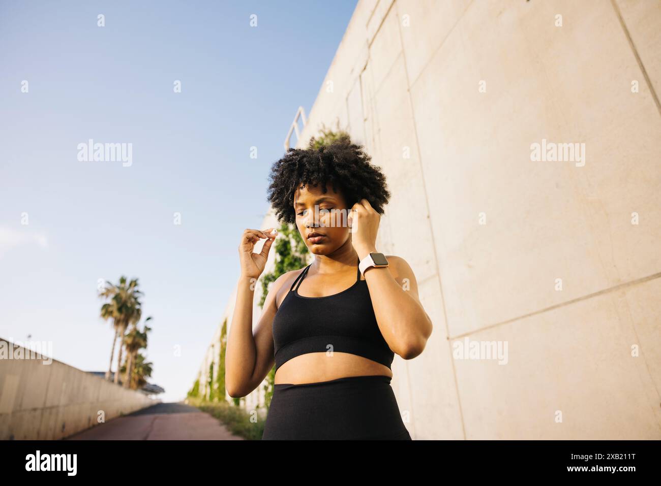 Donna che regola le cuffie mentre si prepara all'allenamento. Giovane donna che indossa abiti sportivi pronta a iniziare la sua routine di allenamento. Foto Stock