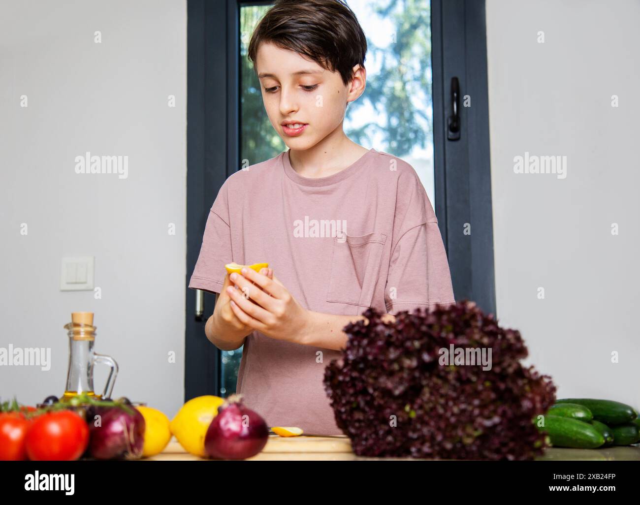 Un ragazzo carino sta guardando il limone nelle sue mani in cucina Foto Stock