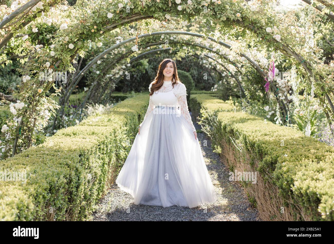 Donne gioiose che camminano in giardino sotto i fiori in abito blu ardesia Foto Stock