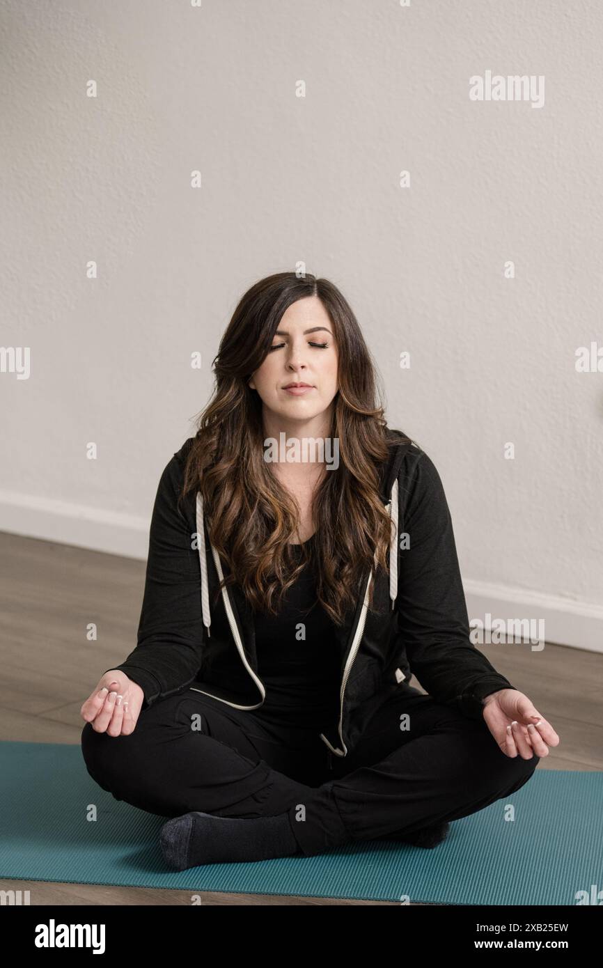 Donne sedute in possesso di yoga sul tappetino con gli occhi chiusi Foto Stock