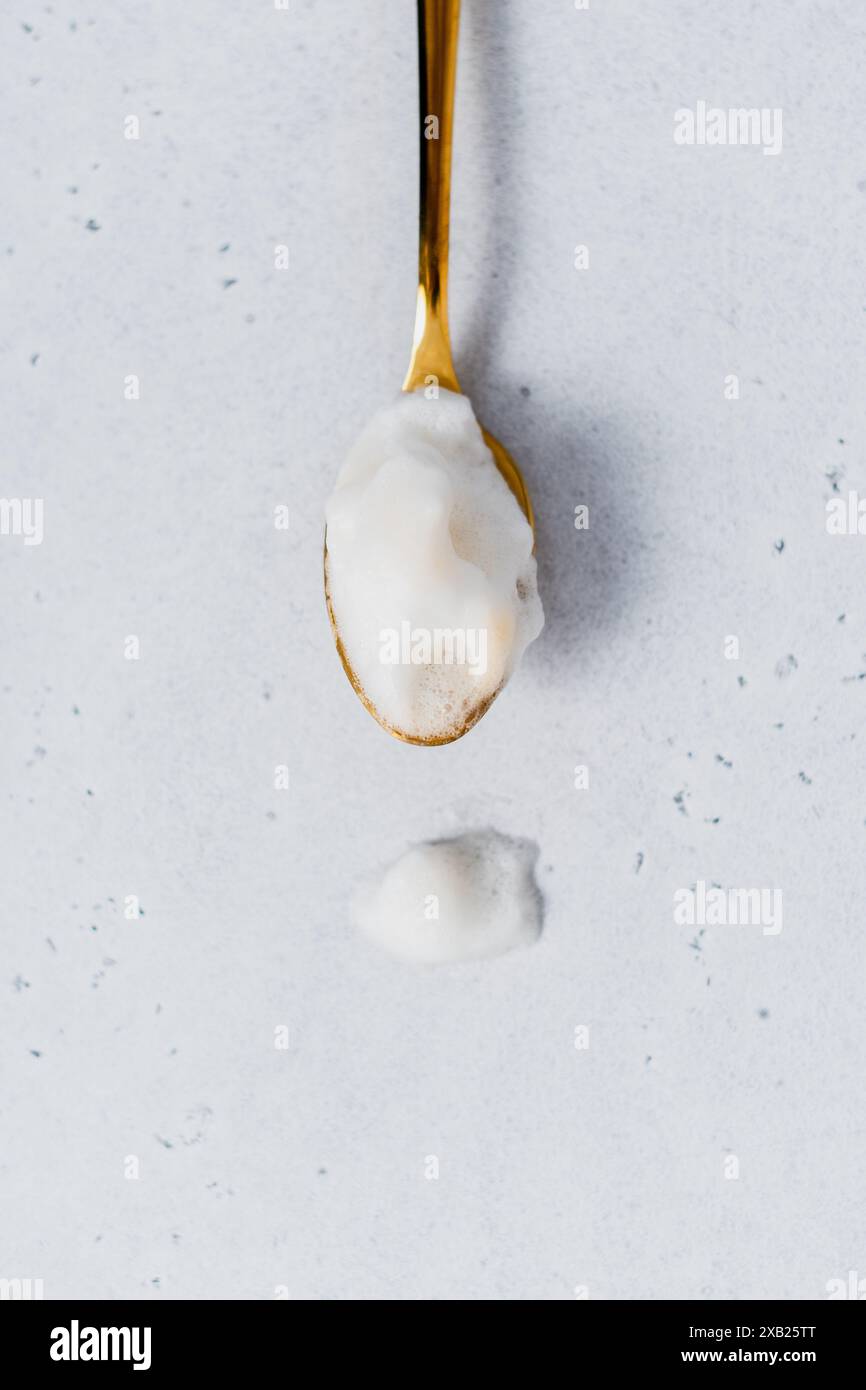Primo piano di un cucchiaio di tè dorato riempito di schiuma di latte Foto Stock
