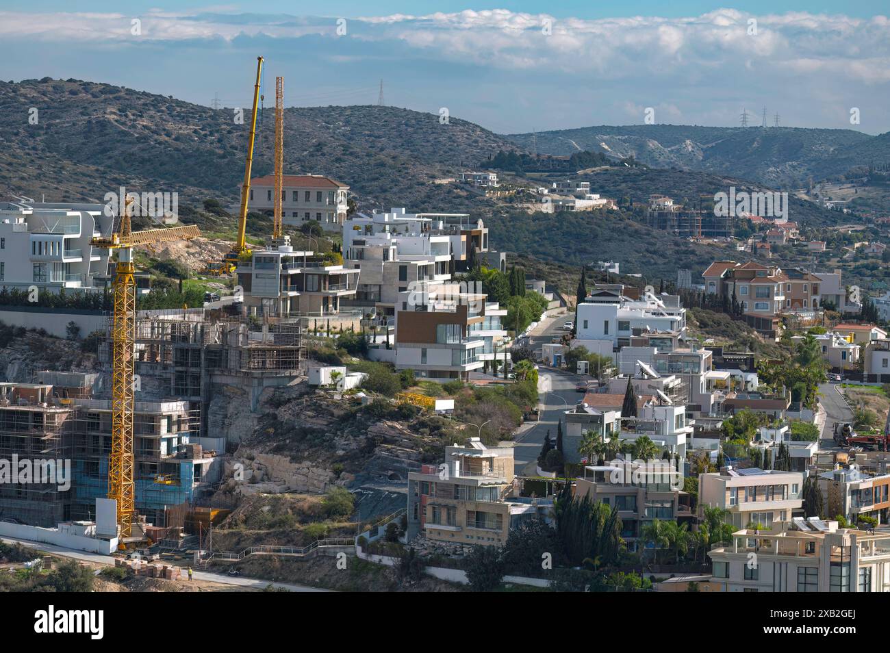 La gru da costruzione sovrasta un'area residenziale in via di sviluppo con case moderne sullo sfondo di una collina. Limassol, Cipro Foto Stock