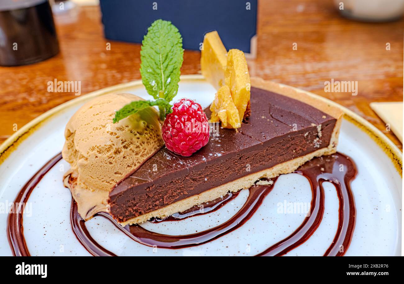 Crostata al cioccolato con gelato, lampone, menta e guarnizione di frutta, elegantemente placcata in un ambiente da caffetteria Foto Stock