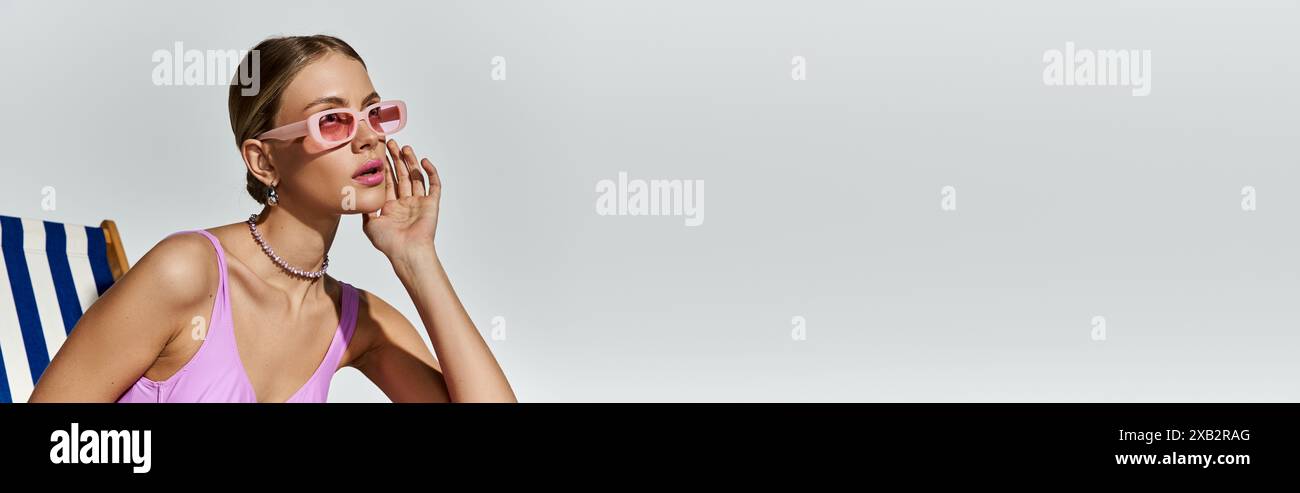 Donna elegante con capelli biondi seduta su una sedia da spiaggia in un bikini rosa. Foto Stock