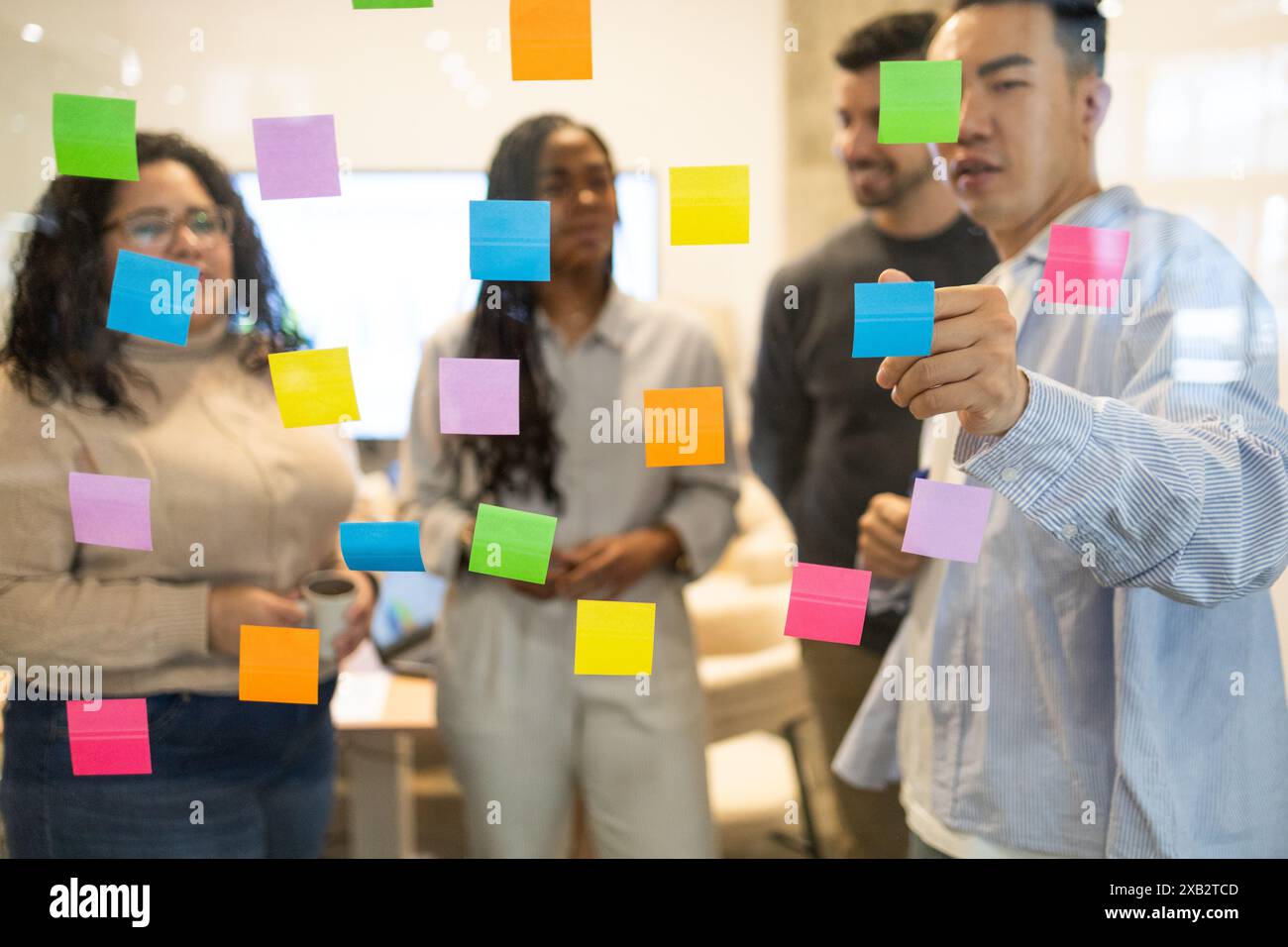 Un gruppo multiculturale di amici collabora con note adesive colorate su una parete di vetro in uno spazio di coworking Foto Stock