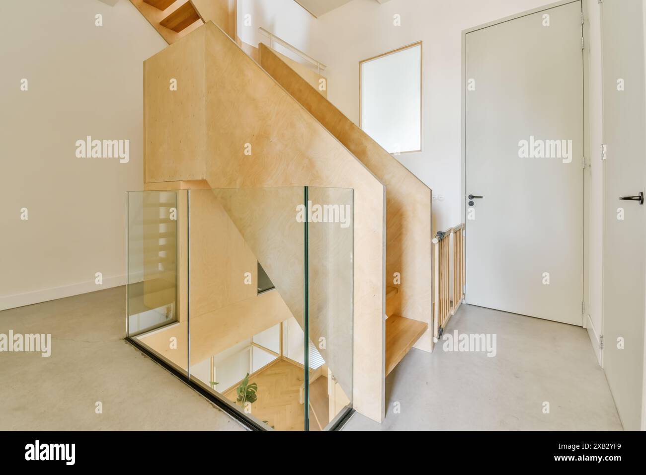 Interni contemporanei con scala in legno con balaustra in vetro, adagiata su uno sfondo bianco minimalista con un tocco di verde. Foto Stock