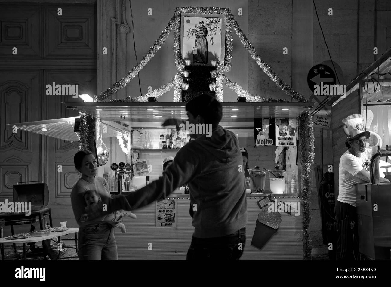 L'uomo balla ubriacatamente di fronte alla moglie e al bambino in una bancarella decorata durante i festeggiamenti di alfama, con un'immagine di San Antonio adornata sopra Foto Stock