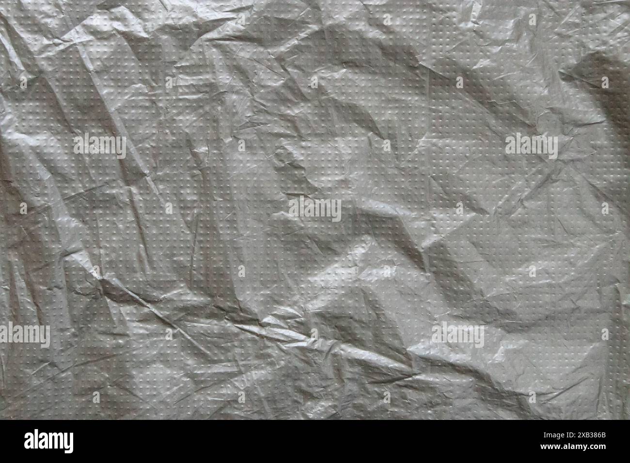 Pellicola in plastica grigio argento con sfondo a punti in rilievo. Trama della pellicola grigia spiegazzata. Sfondo grunge. Foto Stock