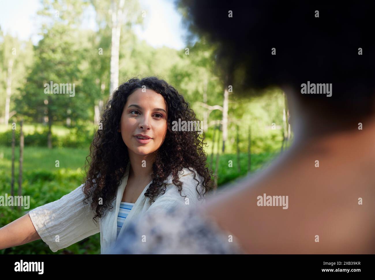 Giovane donna dai capelli ricci che parla con un amico Foto Stock