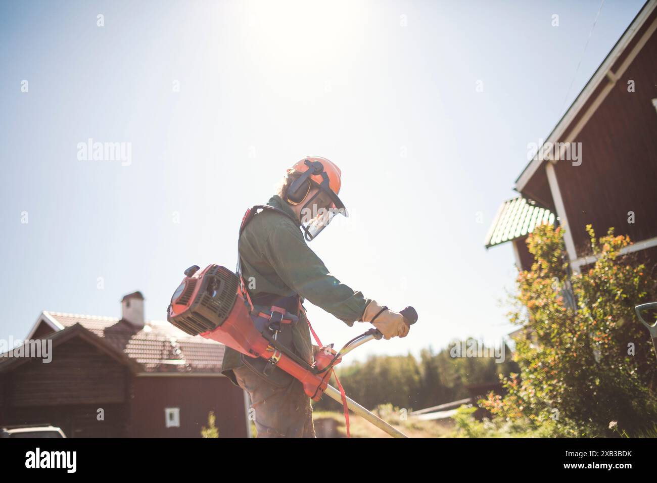 Donna con rifinitore per erbacce nel cortile posteriore contro il cielo durante la giornata di sole Foto Stock
