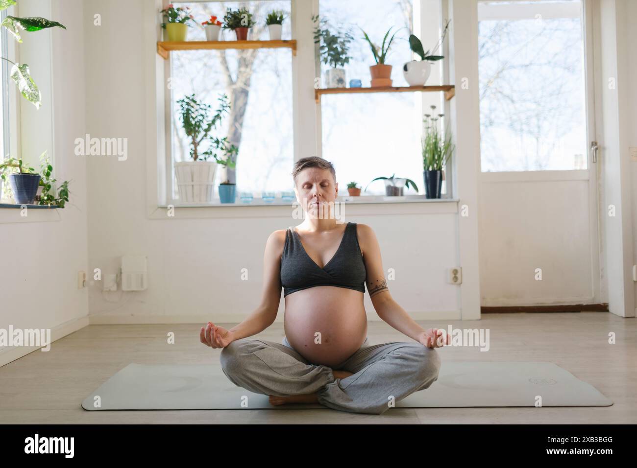 Giovane donna incinta che meditava sul tappetino per esercizi a casa Foto Stock