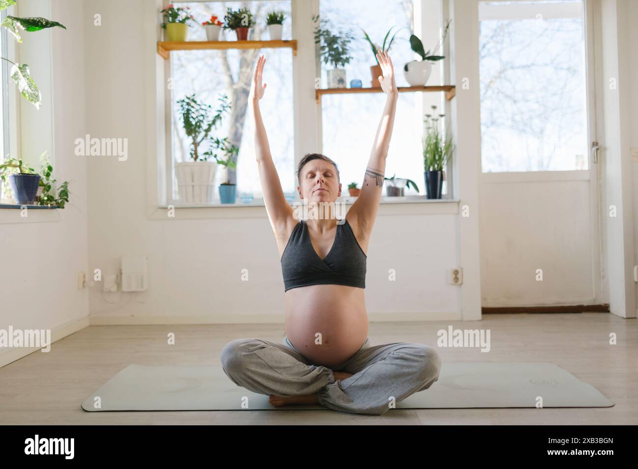 Donna incinta che pratica yoga con le braccia sollevate a casa Foto Stock