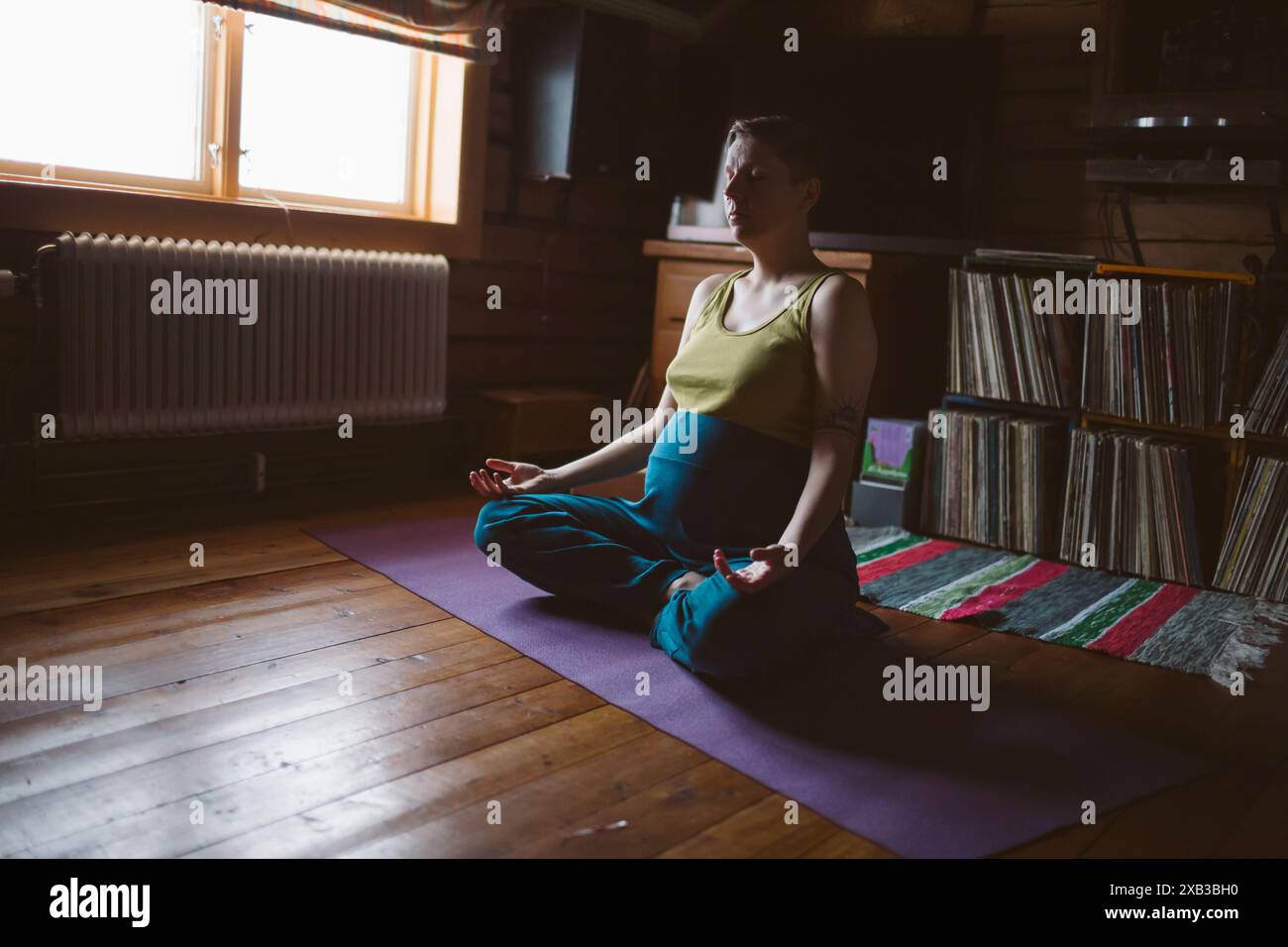 Giovane donna incinta che meditava sul tappeto a casa Foto Stock