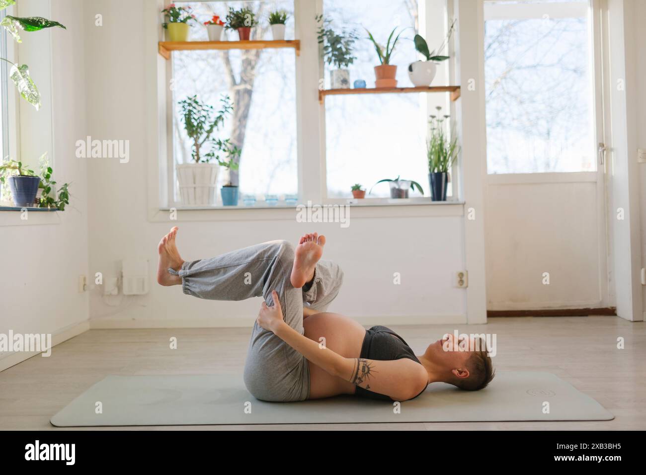 Donna incinta che pratica yoga mentre sdraiata sul tappeto a casa Foto Stock