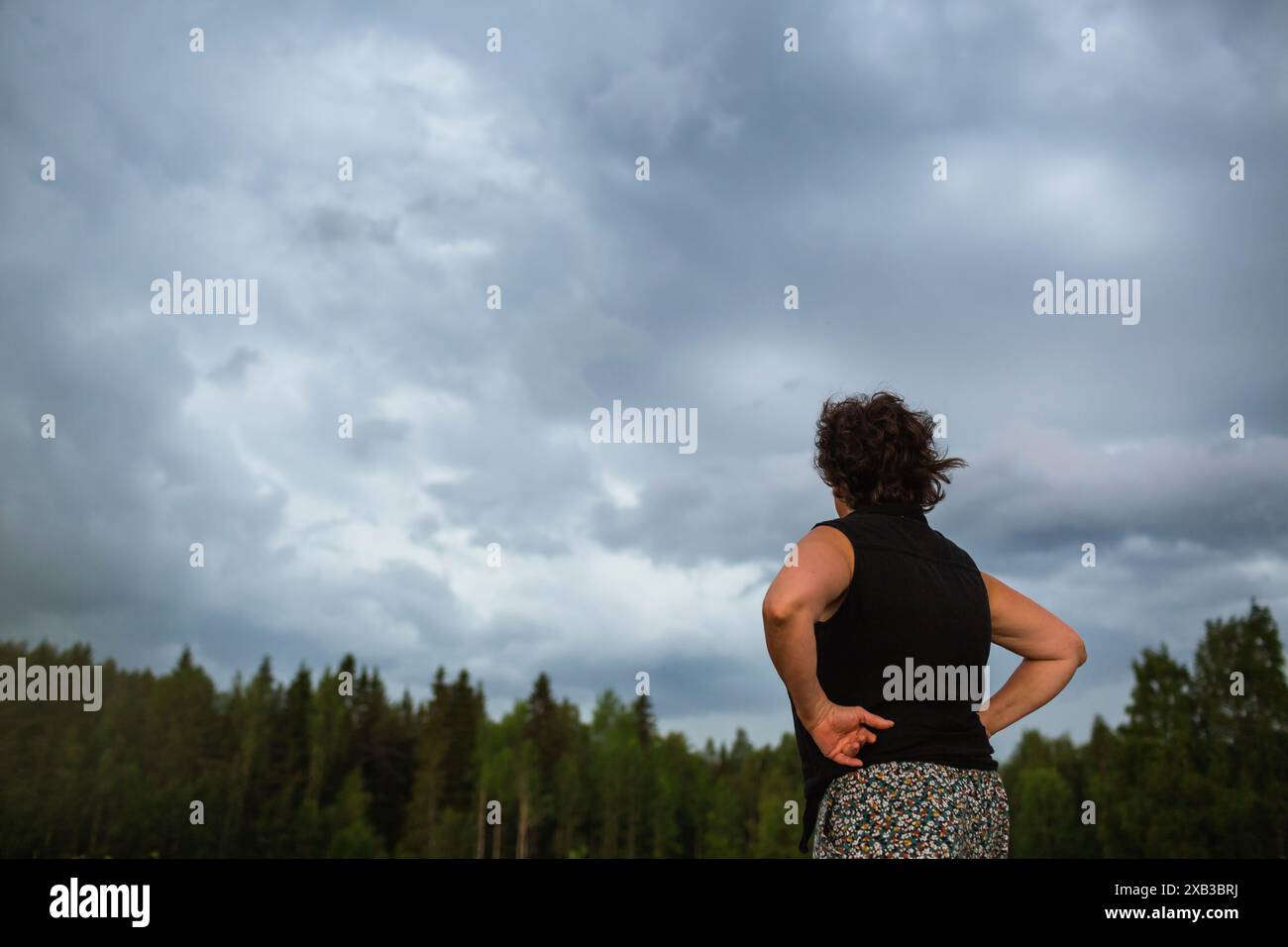 Vista ad angolo basso della donna in piedi con le braccia akimbo e guardando il cielo Foto Stock