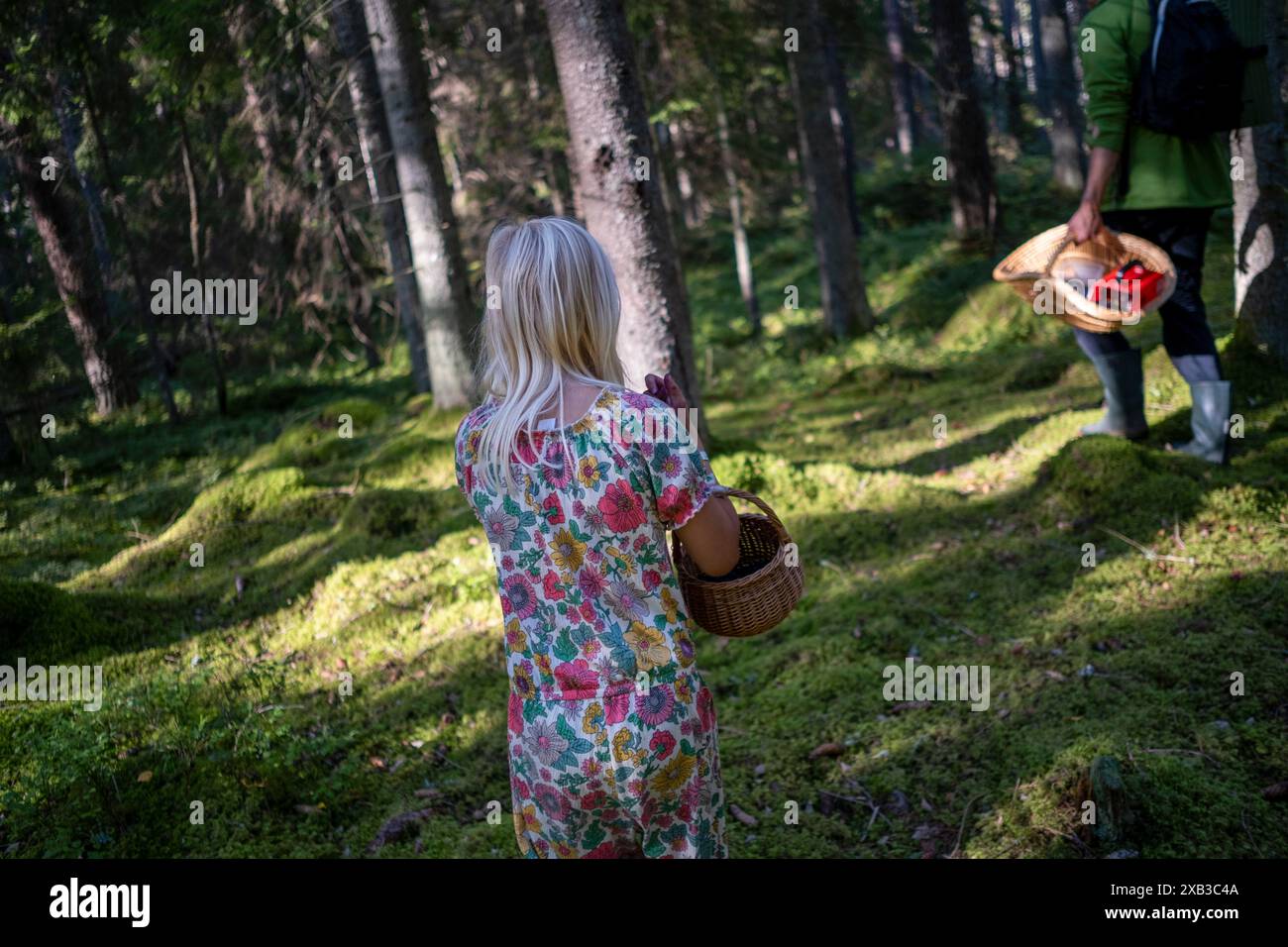 Ragazza che indossa un abito stampato e tiene in mano il cestino mentre cammina nella foresta Foto Stock