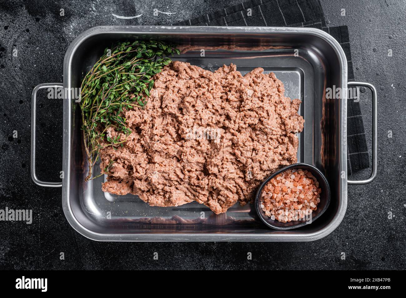 Carne macinata vegetariana, carne a base di piante crude con erbe aromatiche nel vassoio della cucina Sfondo nero. Vista dall'alto. Foto Stock
