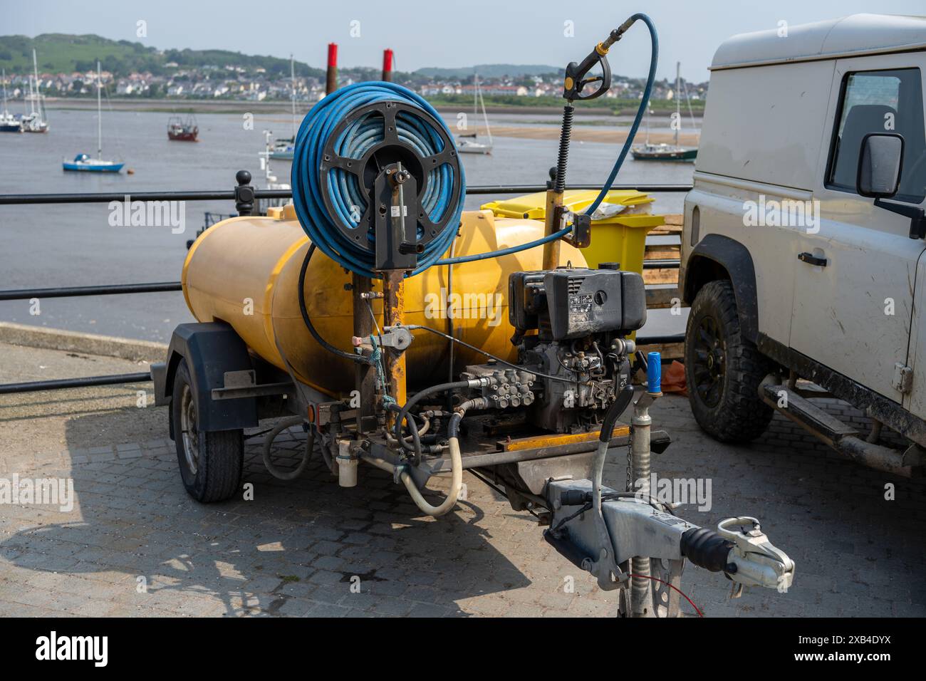 Conwy Wales Regno Unito 06-01-2024. Rimorchio giallo per lavaggio a pressione presso il porto con barche e veicoli commerciali sullo sfondo Foto Stock