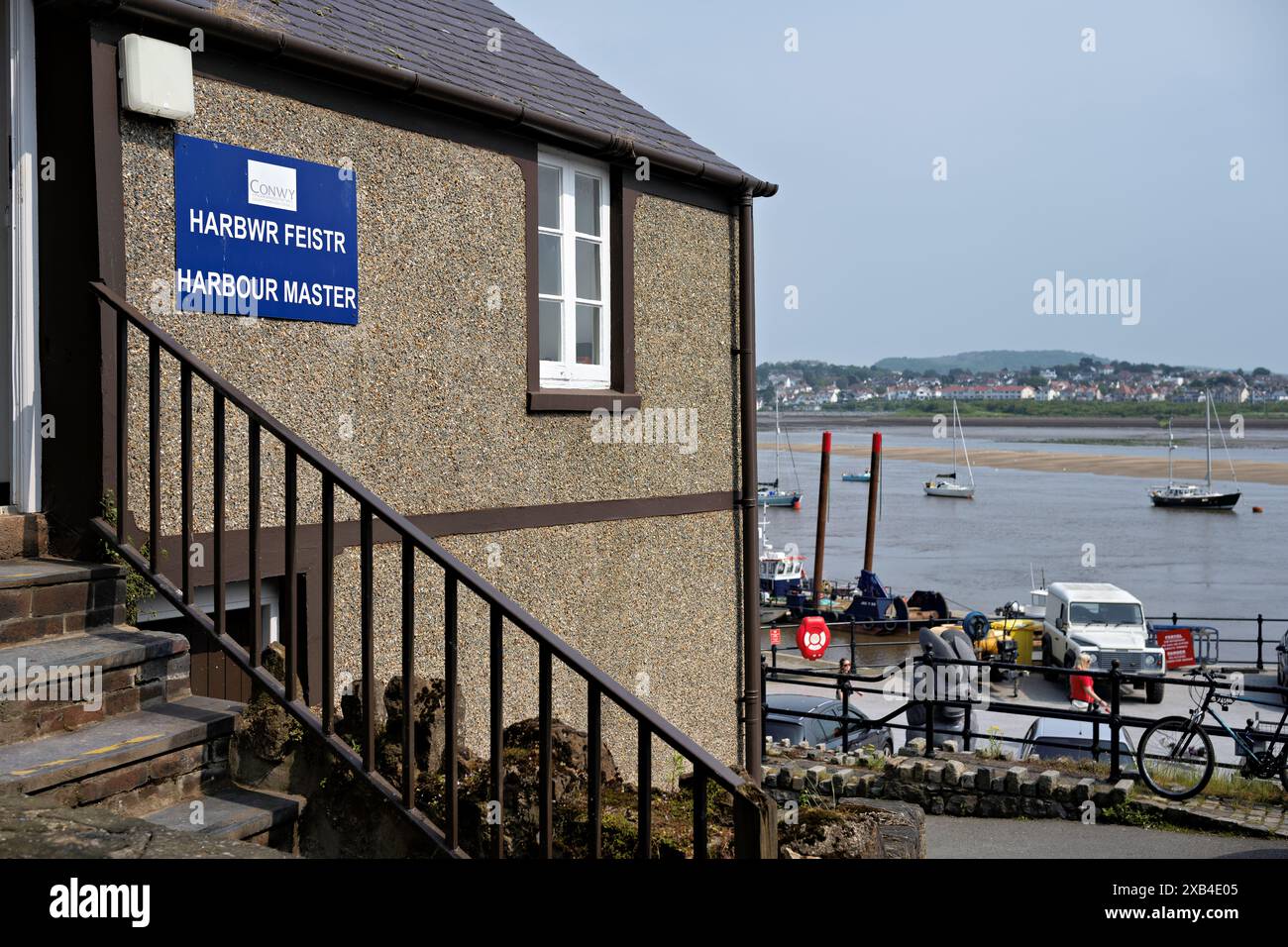 Conwy Wales Regno Unito 06-01-2024. Un pittoresco edificio padronale del porto che si affaccia su un tranquillo porto con barche e un lontano paesaggio urbano. Foto Stock