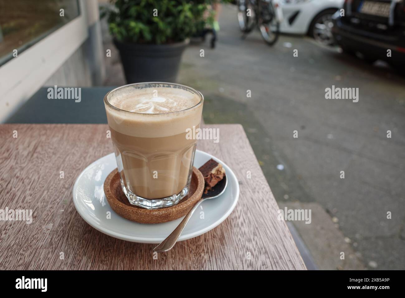 Un latte splendidamente artigianale con delicata latte art si trova su un tavolo di legno in un caffè all'aperto. Foto Stock