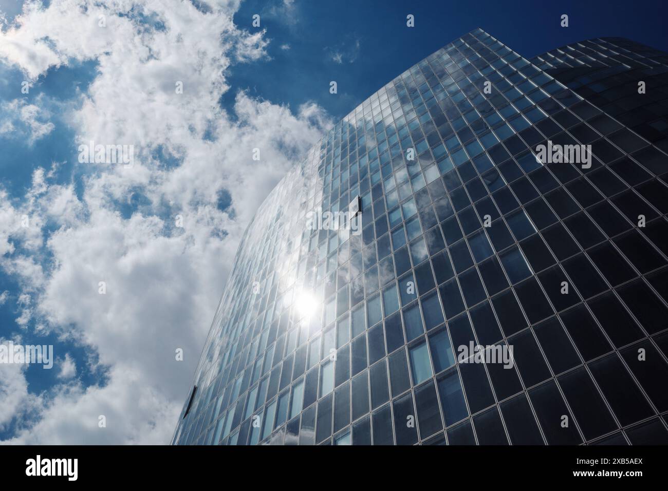 Grattacielo moderno con un'elegante facciata in vetro che riflette il cielo blu luminoso e le nuvole bianche sparse. Foto Stock