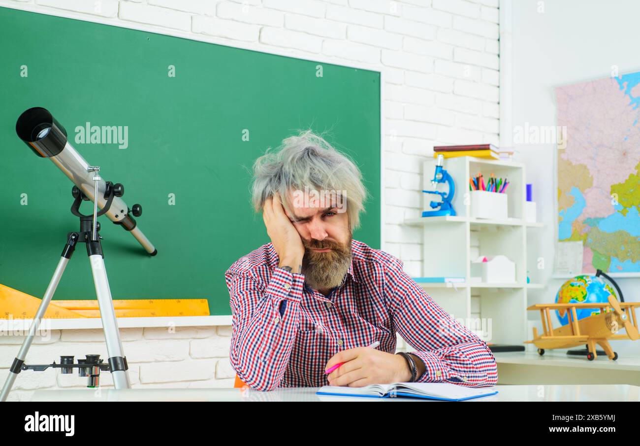 Studente universitario stanco che scrive con la penna in un giornale di carta, prende appunti studiando, facendo i compiti. Un insegnante affaticato prepara le lezioni Foto Stock