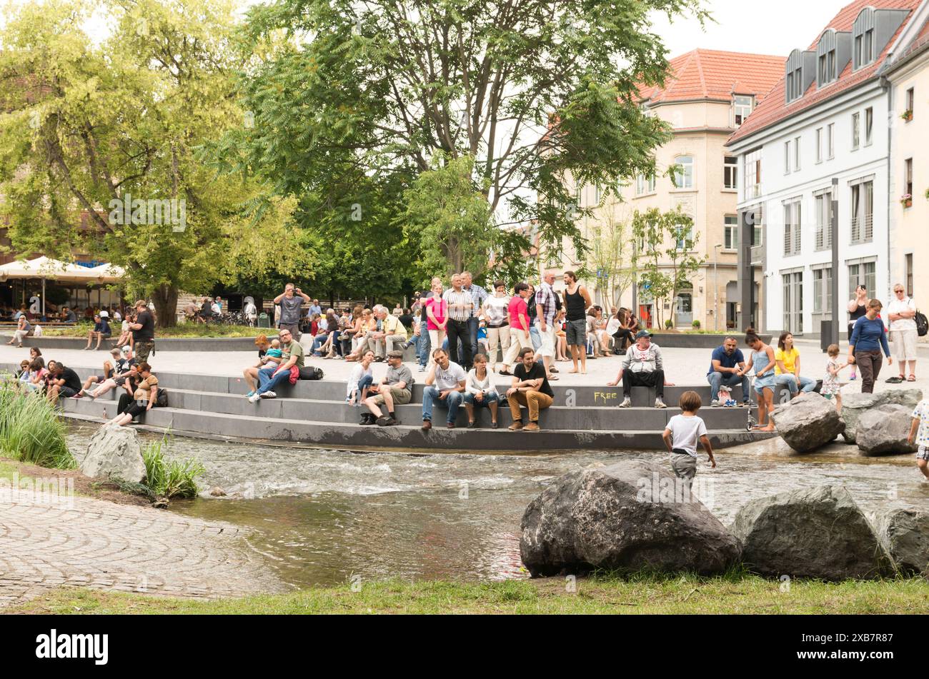Un gruppo di persone sedute su massi vicino all'acqua e al paesaggio urbano Foto Stock