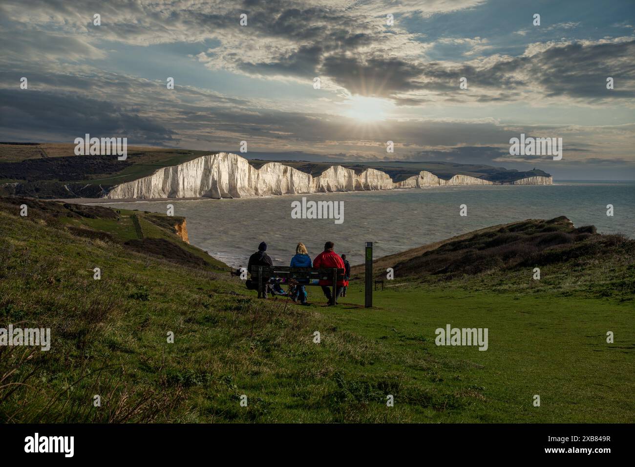 Gruppo di persone sedute su una panchina che si affaccia sul mare vicino alle scogliere Seven Sisters Foto Stock