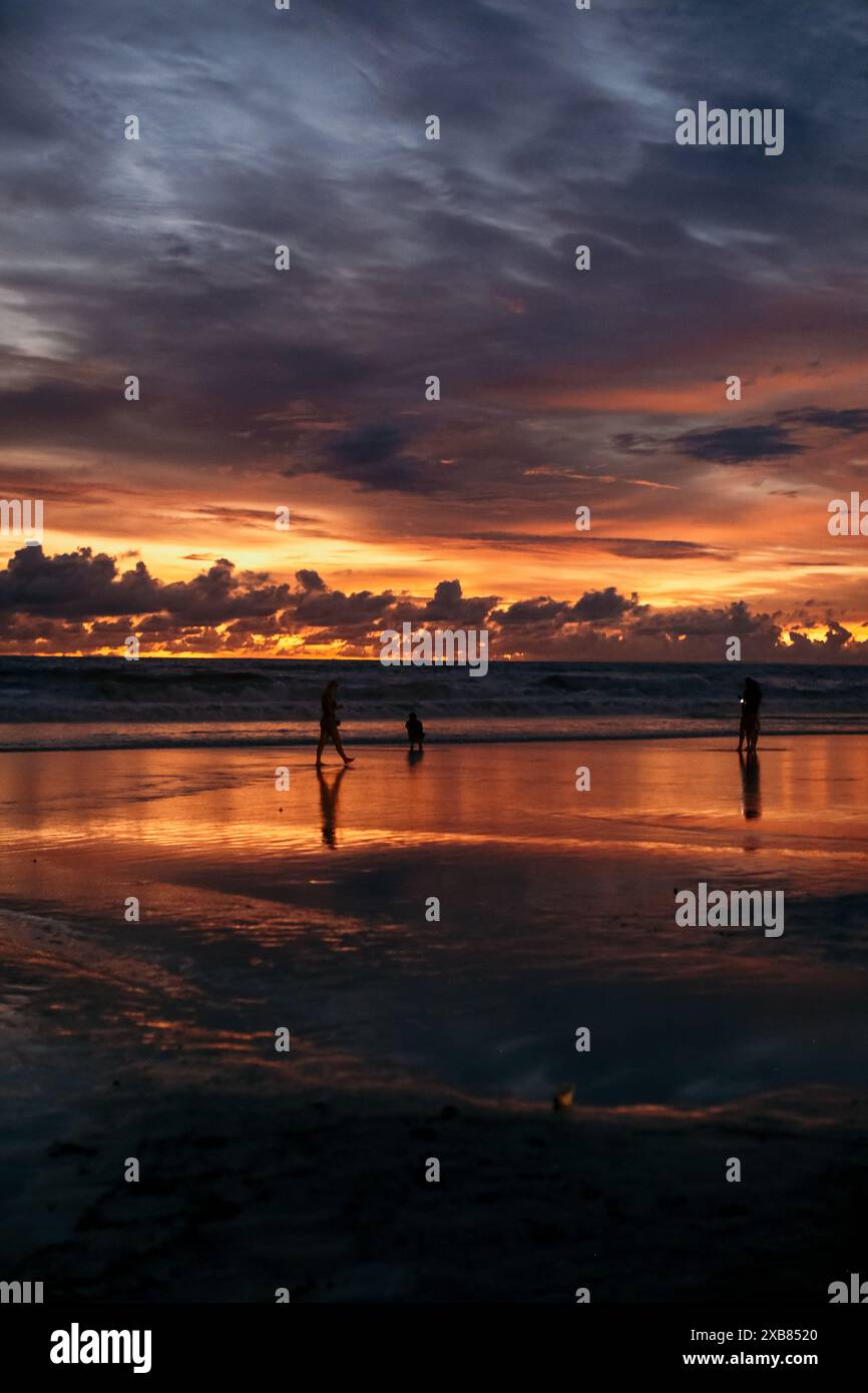 Un gruppo di individui che passeggiano sulla spiaggia in riva all'acqua durante il tramonto a Bali Foto Stock