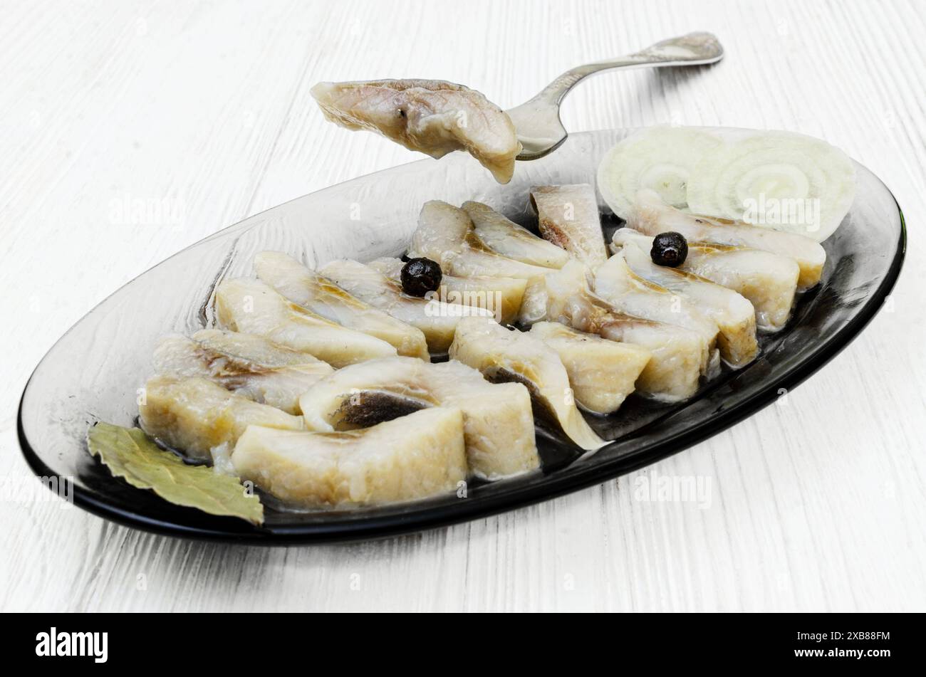 Primo piano. Un piatto da portata in vetro riempito con fette di aringhe sottaceto ordinate, guarnite con fette di cipolla e grani di pepe nero. Foto Stock