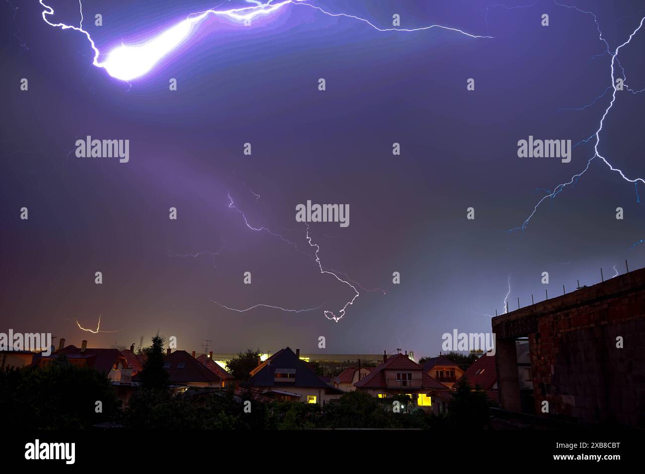Un fulmine colpisce il cielo sopra le case in cima alla collina Foto Stock