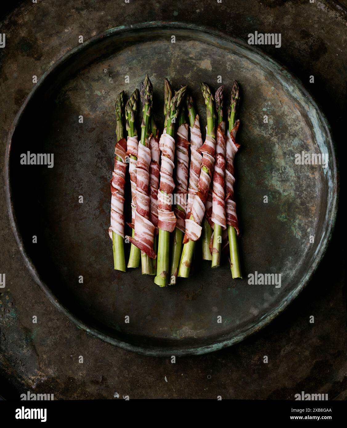 Asparagi avvolti in pancetta disposti in un vassoio rustico e scuro Gli asparagi sono freschi e verdi, ben avvolti con una bacon saporita, creando un'atmosfera visivamente appetitosa Foto Stock