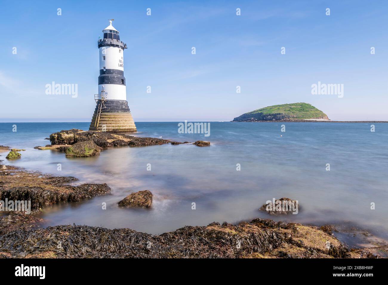 Faro sul bordo di un promontorio roccioso. Il faro si trova a Penmon Point, Angelsey, nel Galles settentrionale. La giornata è soleggiata Foto Stock