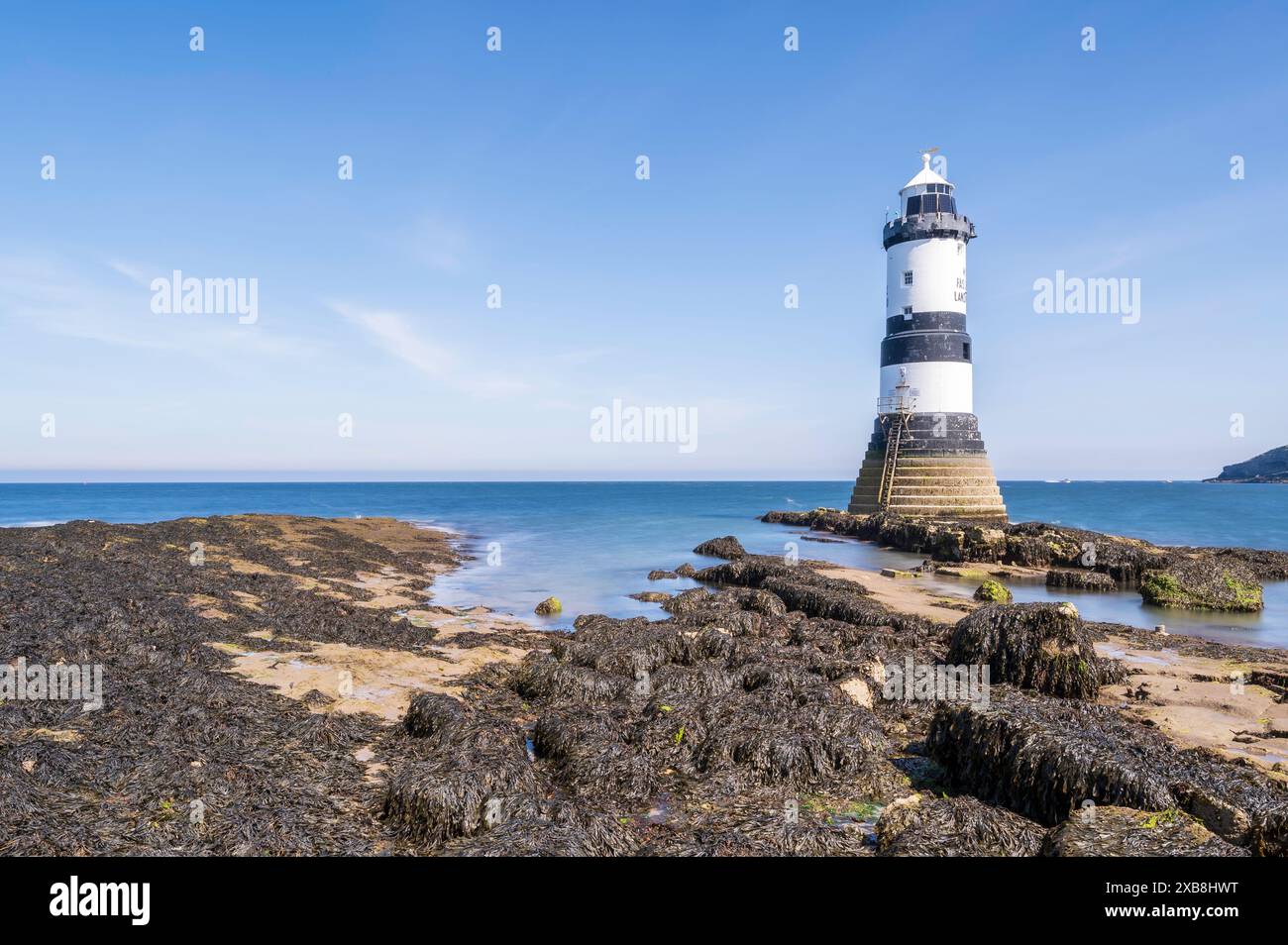 Faro sul bordo di un promontorio roccioso. Il faro si trova a Penmon Point, Angelsey, nel Galles settentrionale. La giornata è soleggiata Foto Stock