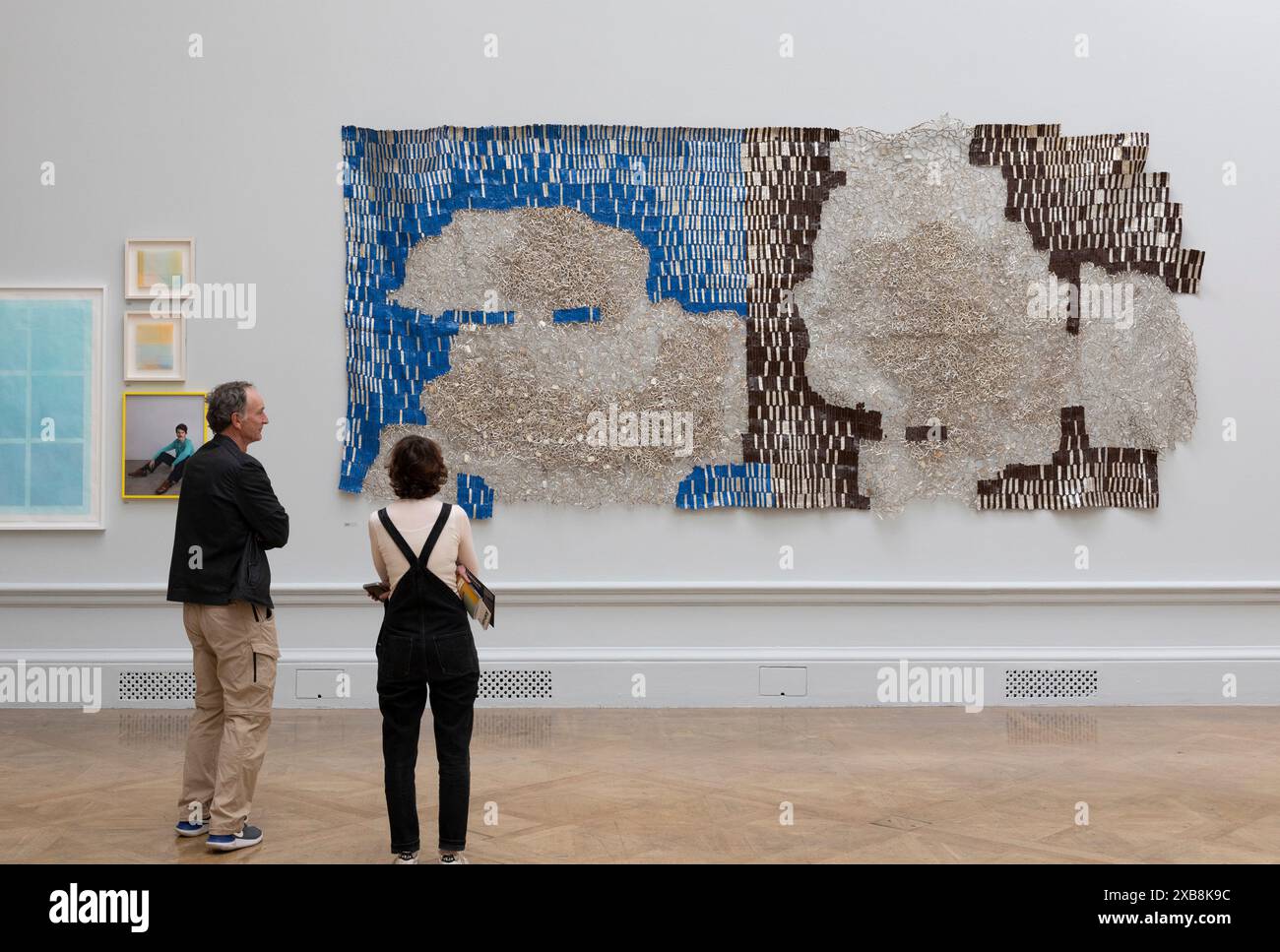 Royal Academy, Londra, Regno Unito. 11 giugno 2024. Quest'anno sono in mostra oltre 1200 opere d'arte, tra cui una straordinaria scultura tessile monumentale nel cortile Annenberg di Nicola Turner, che interagisce con la statua del presidente fondatore della RA, Sir Joshua Reynolds. La mostra estiva presso l'RA di Londra, si svolge dal 18 giugno al 18 agosto 2024 ed è la più grande mostra di arte contemporanea aperta al mondo che si svolge ogni anno senza interruzioni dal 1769. Immagine: Continenti in gestazione di El Anatsui, Hon RA. Un lavoro su larga scala in alluminio e rame Foto Stock