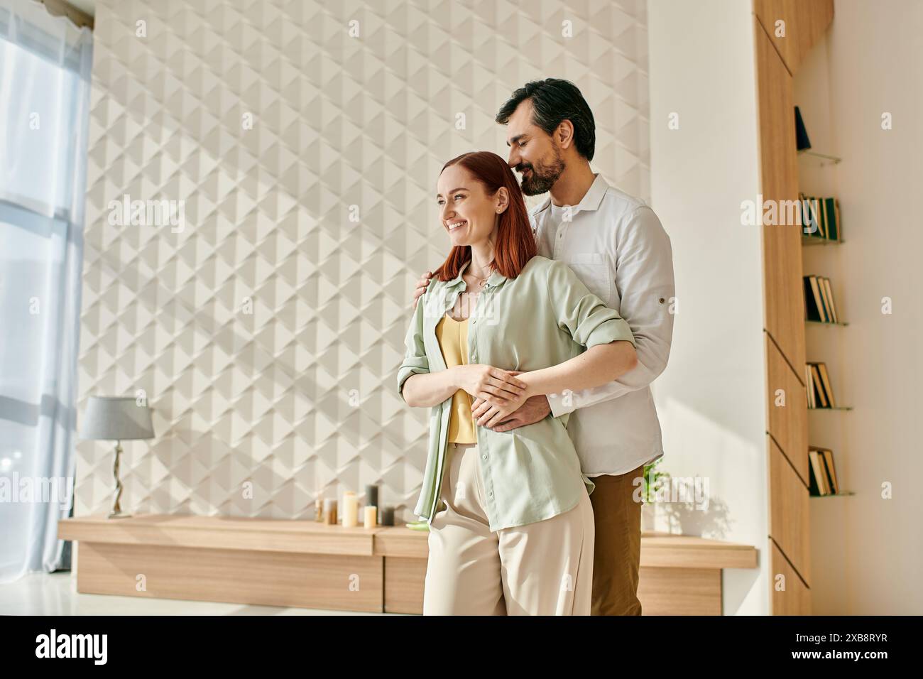 La donna rossa e l'uomo barbuto stanno insieme in un salotto moderno, trascorrendo del tempo di qualità in un ambiente accogliente. Foto Stock
