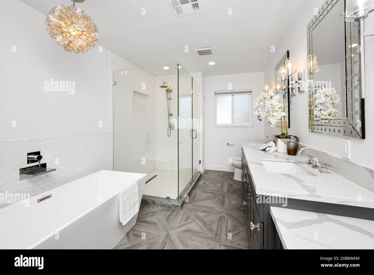 Bagno elegante e moderno con pavimenti in legno, ripiani in marmo, vasca bianca e due lavandini Foto Stock
