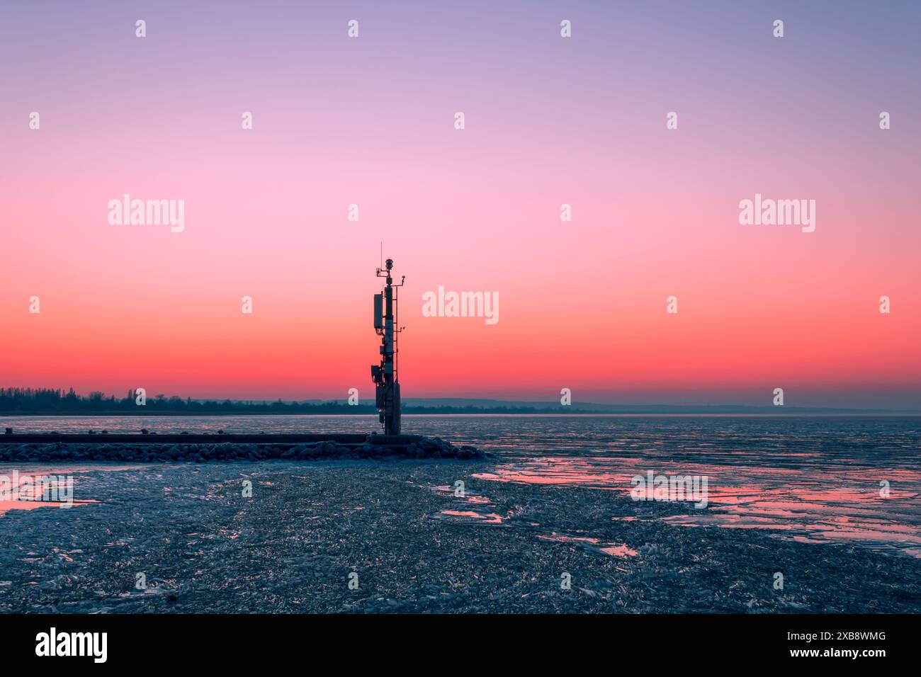 Un tramonto tranquillo dipinge il cielo sopra una torre solitaria vicino all'acqua. Foto Stock