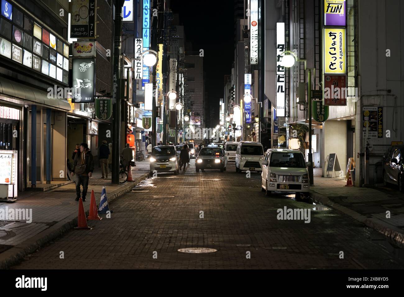 Strada urbana trafficata con auto e gente di notte nel quartiere della città Foto Stock