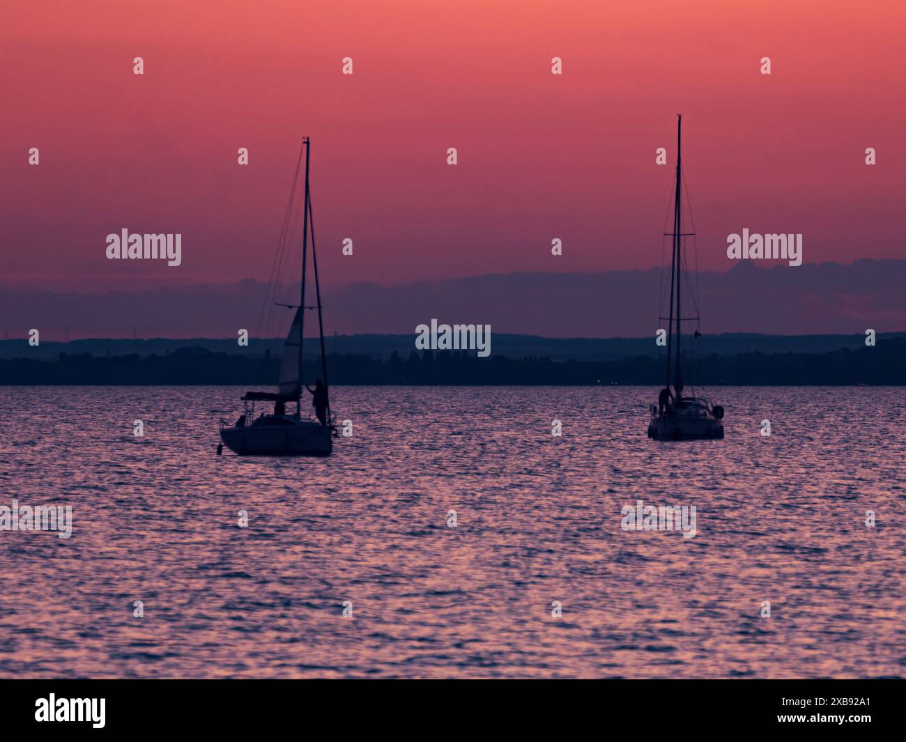 L'immagine cattura una scena serena con due barche a vela sull'acqua durante il tramonto. Foto Stock