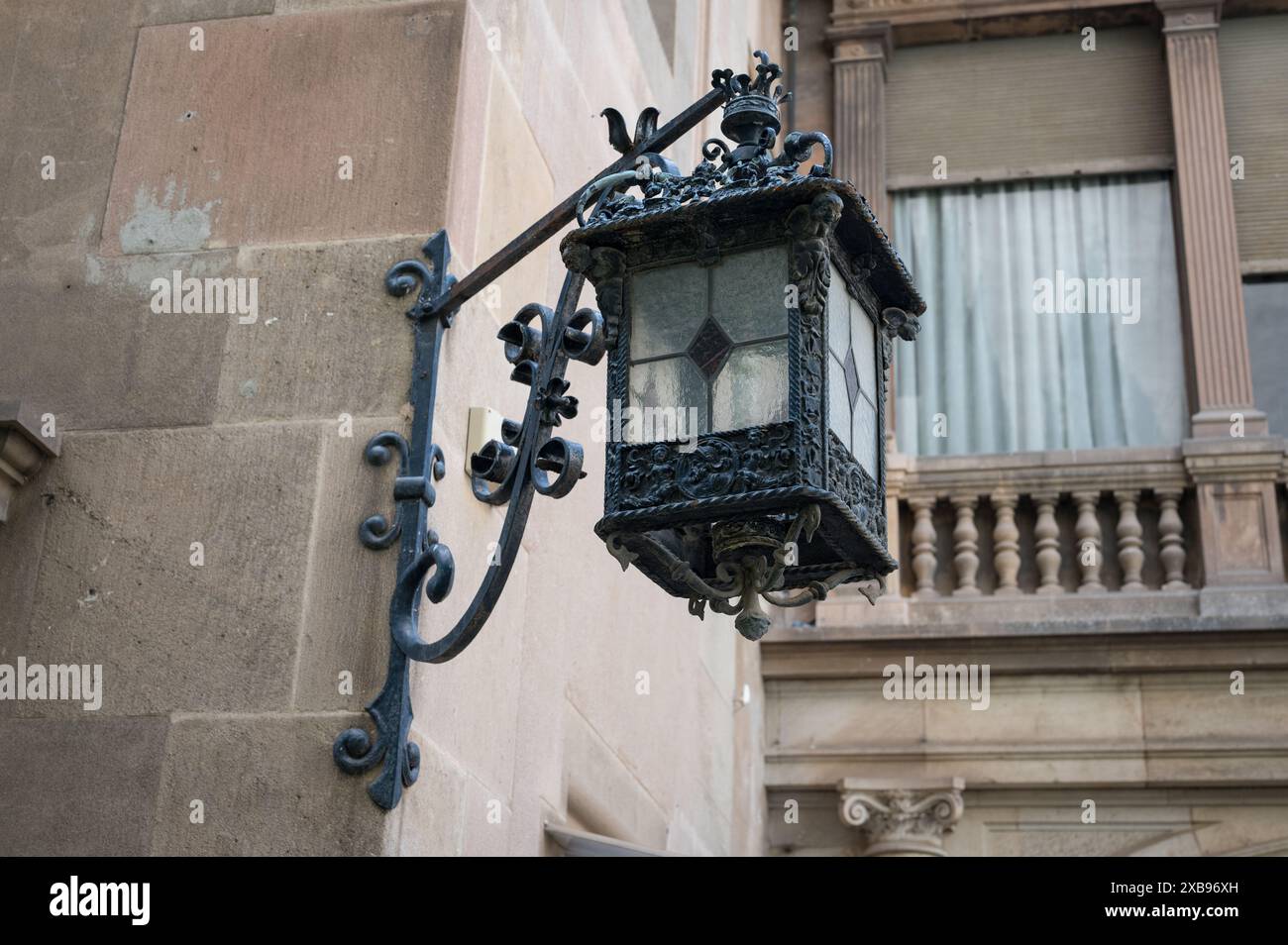 Particolare di una vecchia lampada in ferro battuto decorata collocata nell'angolo di una facciata in pietra con supporto angolare. E' quadrato e carino Foto Stock