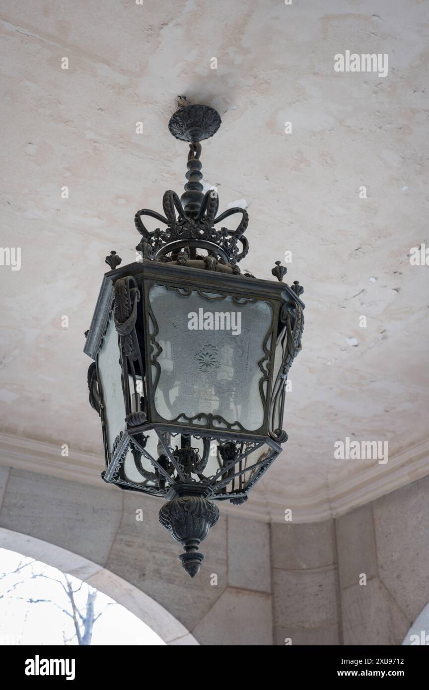 vecchia e ornata lampada in ferro battuto appesa al soffitto. E' di forma quadrata e si trova in un vecchio edificio dall'architettura di Barcellona. Foto Stock